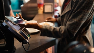 Eine junge Frau bezahlt an der Kasse kontaktlos mit dem Smartphone, ohne Portemonnaie.